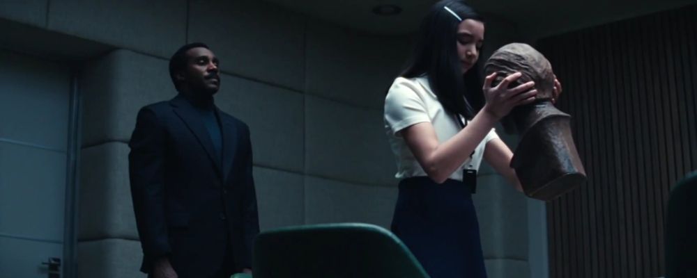 screencap from severance. miss huang is lifting her trophy with mr. milchick observing. 