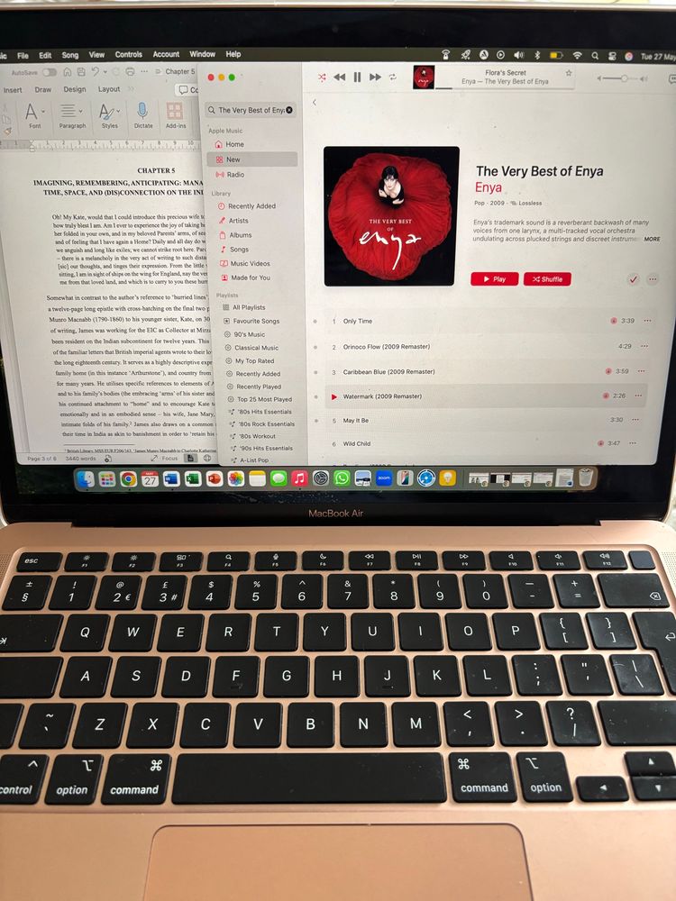 Photo of laptop screen showing a word document on one side and Apple Music on the other, with Enya playing.