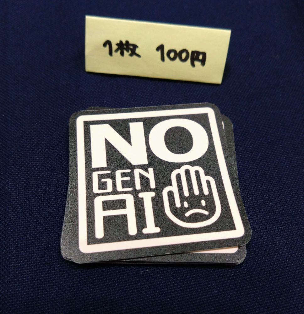 机に置かれたシールと値札の写真。シールにはNO GEN AIという文字と手のひらに怒った様な顔が描かれたイラストが書かれている。値札には1枚100円と書かれている。