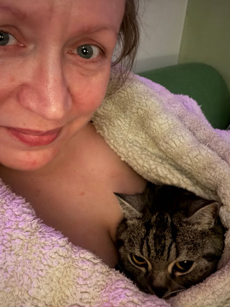 Nærbillede af min kat Luna og jeg. Luna ligger op af mig under min vamsede, hvide fleecekåbe. 