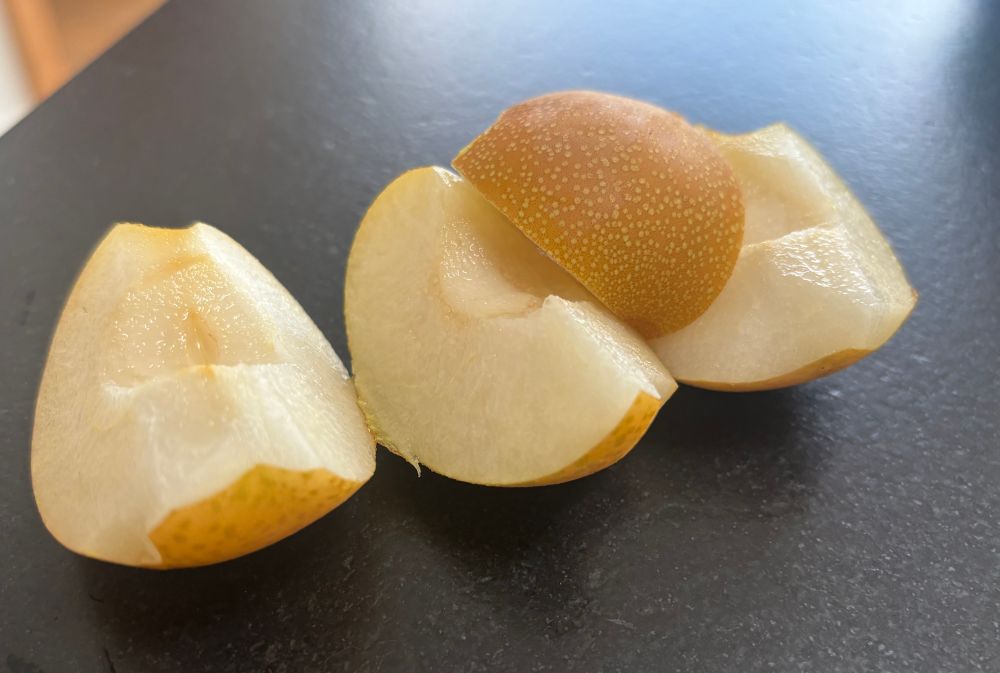 Kleine gelbe Nashi Birne geviertelt auf schwarzer Arbeitsplatte