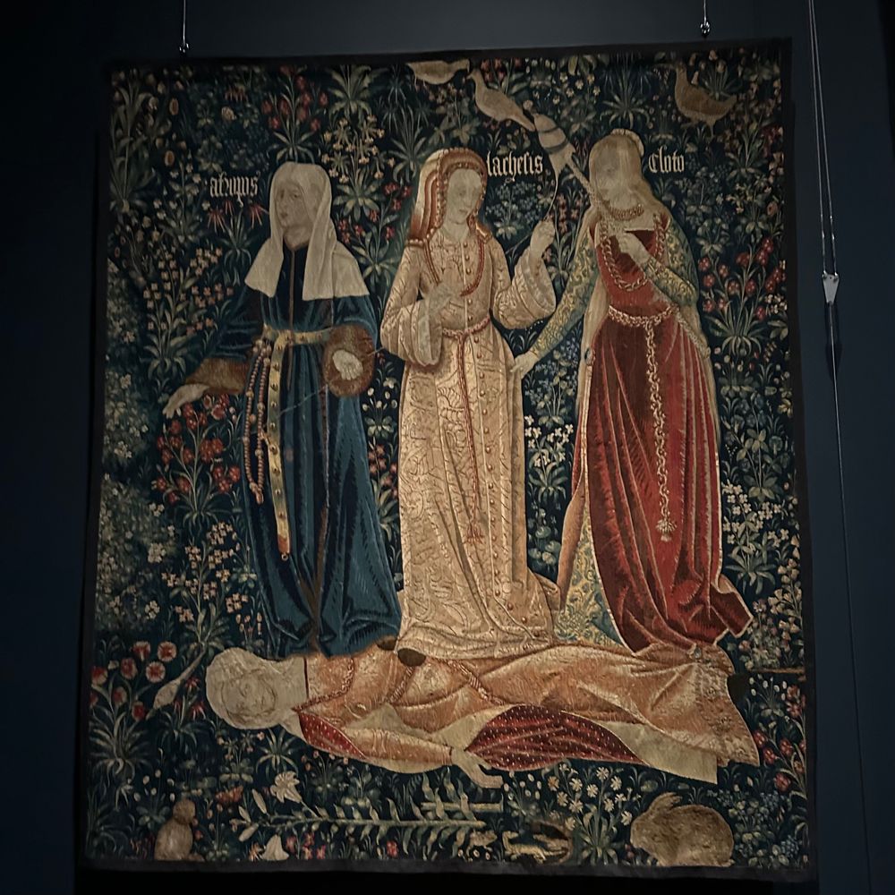 The Three Fates tapestry at the Victoria and Albert Museum. It features three women doing spinning tasks while standing over a fourth dead woman 