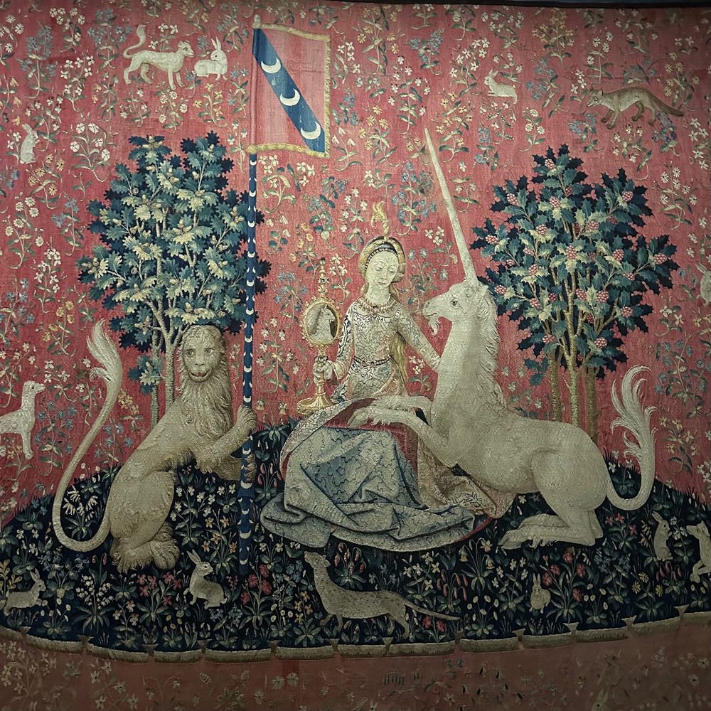 One of the Lady and the Unicorn tapestries at the Cluny Museum. It features a lady showing a unicorn it’s reflection in a mirror, while a lion holds a flagpole 