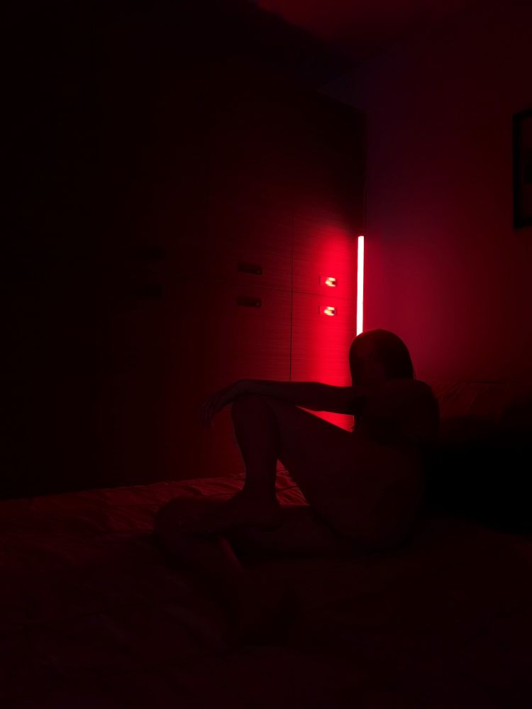 Red lighting showing a black silhouette laying in bed with an arm resting on a knee that's propped up.