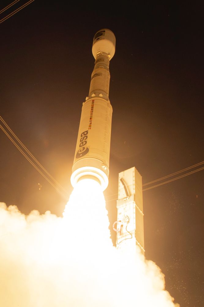 Close up of Vega VV25 rocket launch, illumination gold and orange, black night sky. 
