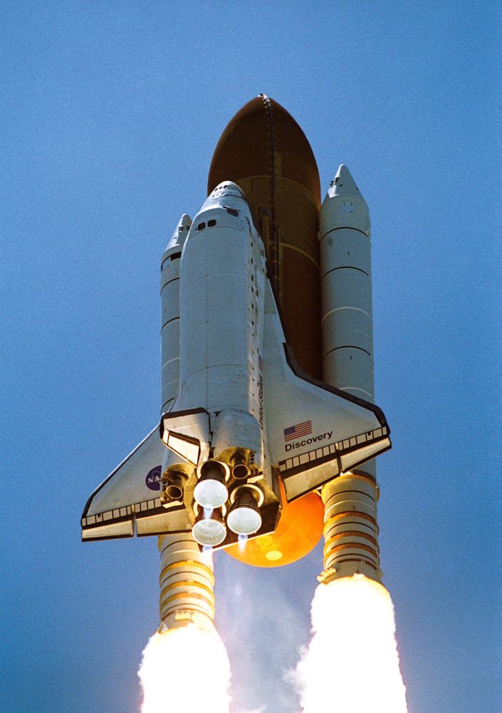 Close-up view of Discovery STS-121 launch with exhaust plumes and rocket engine shock diamonds, orange fuel tank and blue sky