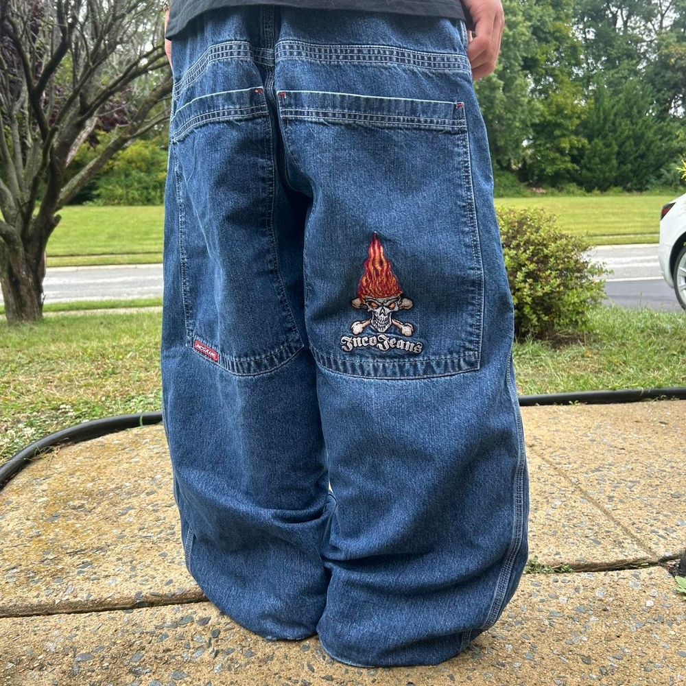 Person wearing blue baggy JNCO jeans.  Giant pockets and a patch with a cartoon skull and crossbones with its hair on fire.  
