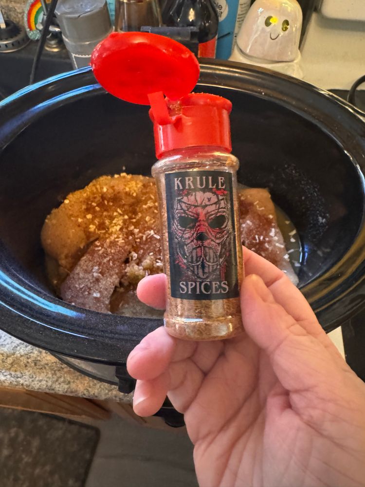 Spices labeled krule spices with chicken in a slow cooker behind it