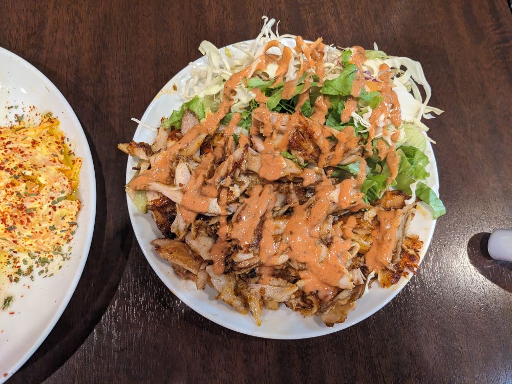 ビーフマトンケバブとレタス、キャベツにピンク色のソースがかかった料理が白い皿に盛られている。隣に別の料理の一部が見える。