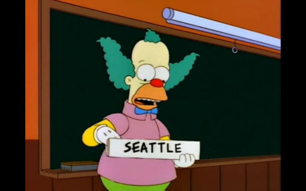 Krusty the Clown holding a sign that reads "Seattle"