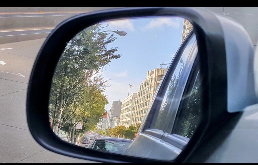 Buildings topped by blue sky with a few clouds in car mirror
