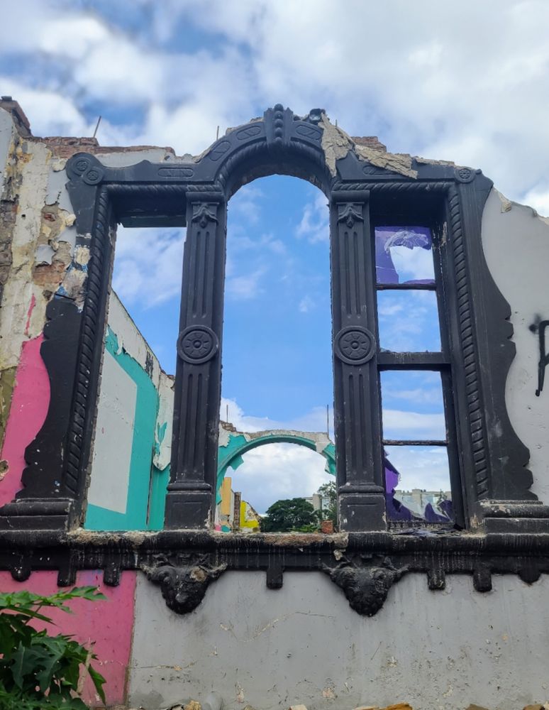 Ruined building with ornate widow frame looking up into blue sky with clouds.