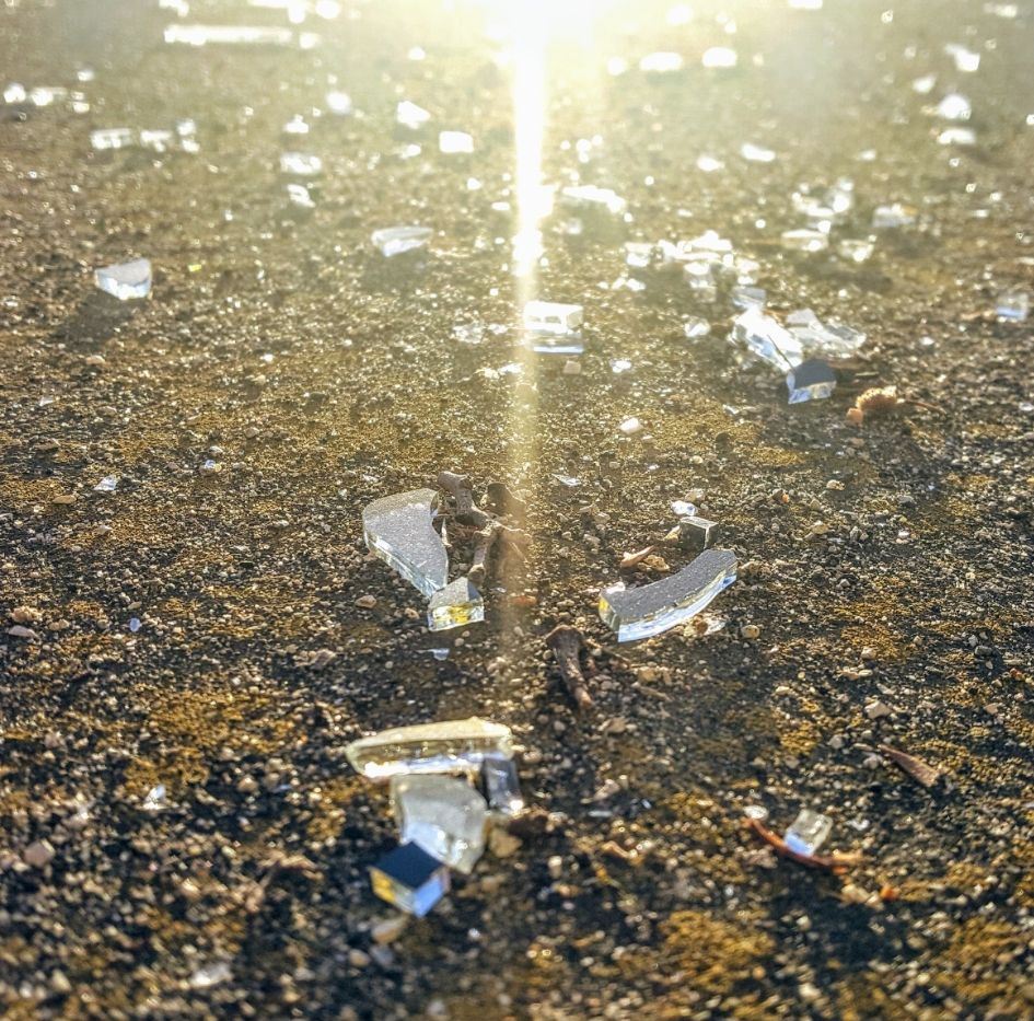 Close up view of shatter glass on asphalt parking lot with sun shining on glass shards.