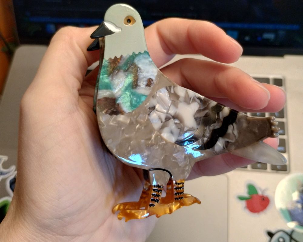 A hand holding a hair clip shaped and decorated to look like a pigeon 