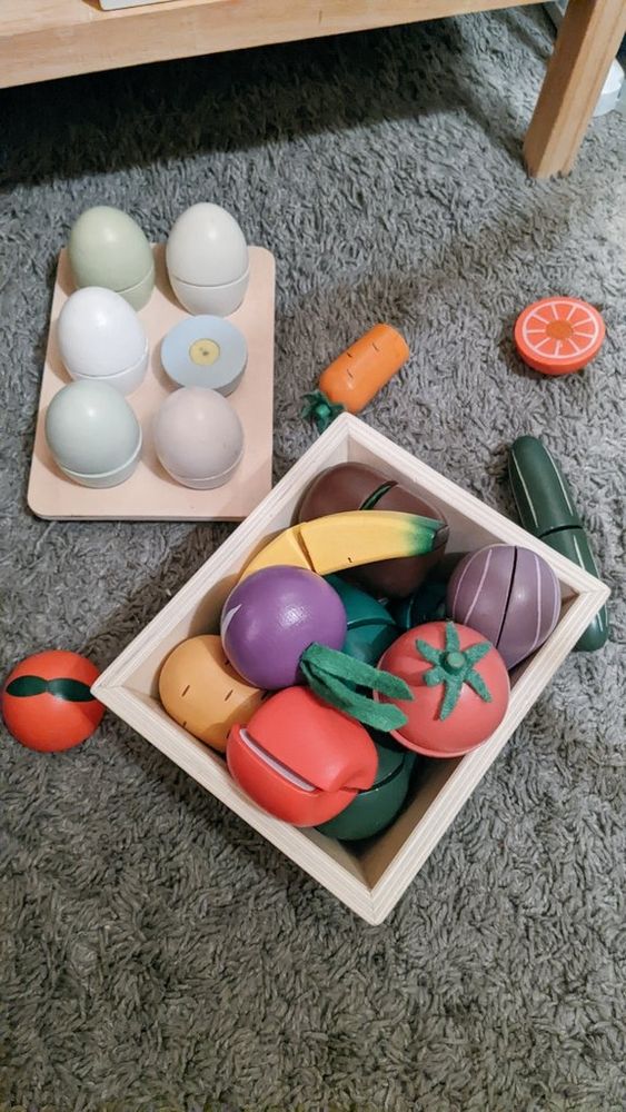 A collection of toy foods in a wooden box, including eggs, fruits, and vegetables.