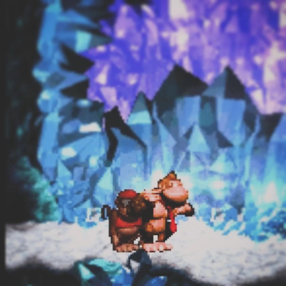 Donkey Kong bangs on his chest whilst standing next to his companion, Diddy Kong, in a blue and purple crystal ice cave.
