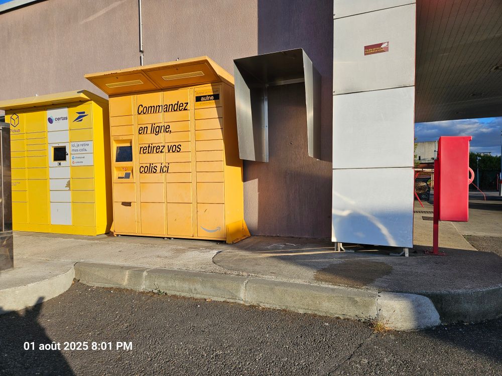 Vue rapprochée des casiers Pickup jaunes avec l'inscription "Commandez en ligne, retirez vos colis ici" et un distributeur de sacs plastique rouge. Les casiers sont installés sur un trottoir sans rampe d'accès, créant un obstacle physique pour les personnes en fauteuil roulant. Aucun seuil de moins de 2 cm chanfreiné aux deux tiers n'est visible, violant les normes d'accessibilité en vigueur depuis la loi de 2005.