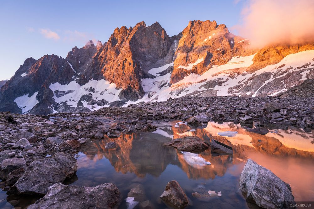 The jagged peaks of Roche Méane (3,712 m / 12,178 ft) reflect in Lac du Pavé at sunrise in Parc National des Écrins, France.