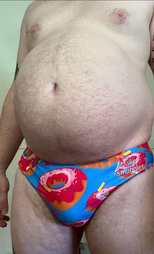 Close up of a round gut protruding over some tight, donut print, budgy smugglers. 