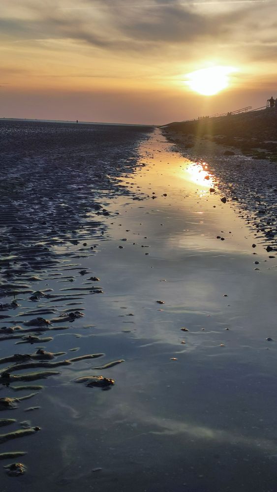 Foto des Sonnenuntergangs, der sich im Restwasser der Ebbe spiegelt