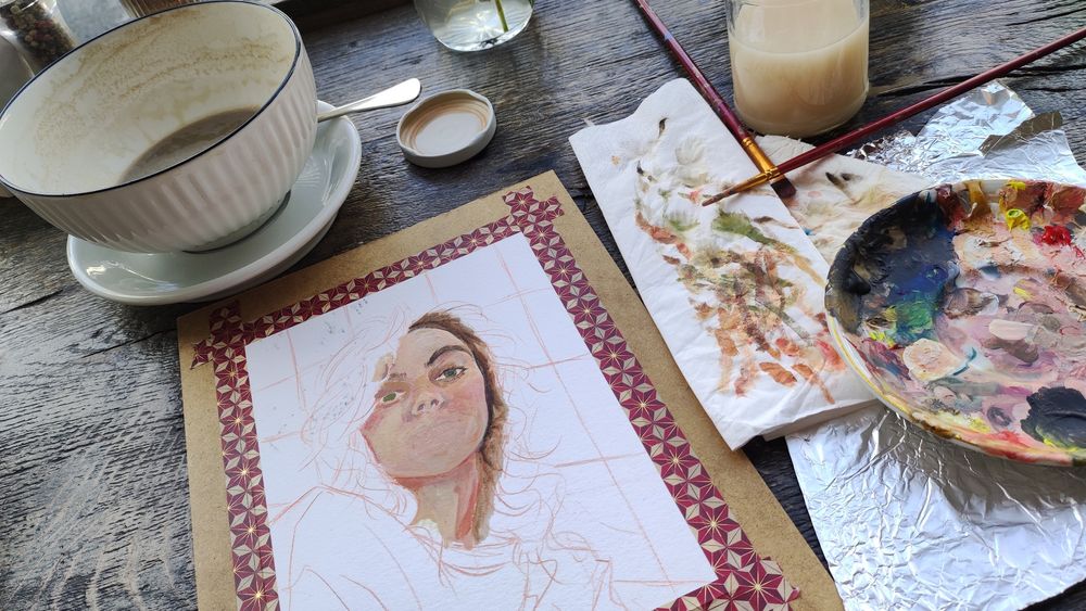 Foto in einem Cafe mit großer Kaffeetasse, vor der Acryl-Equipment und eine angefangene Malerei liegen.