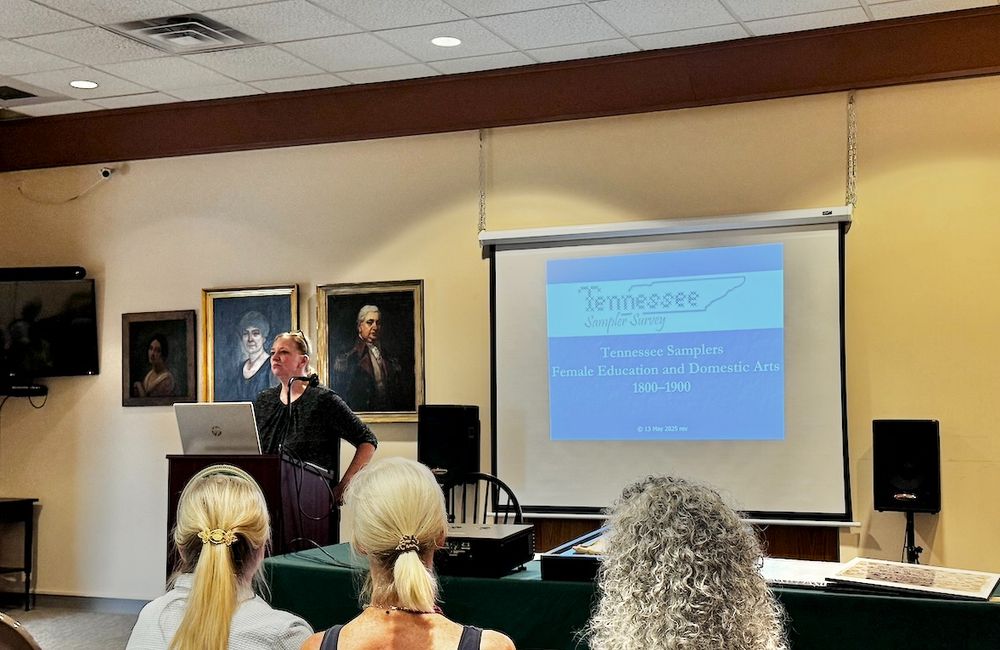 Author Jennifer Core stands at the front of a room in the Blount Mansion visitor's Center with a powerpoint slide that reads "Tennessee Sampler Survey".