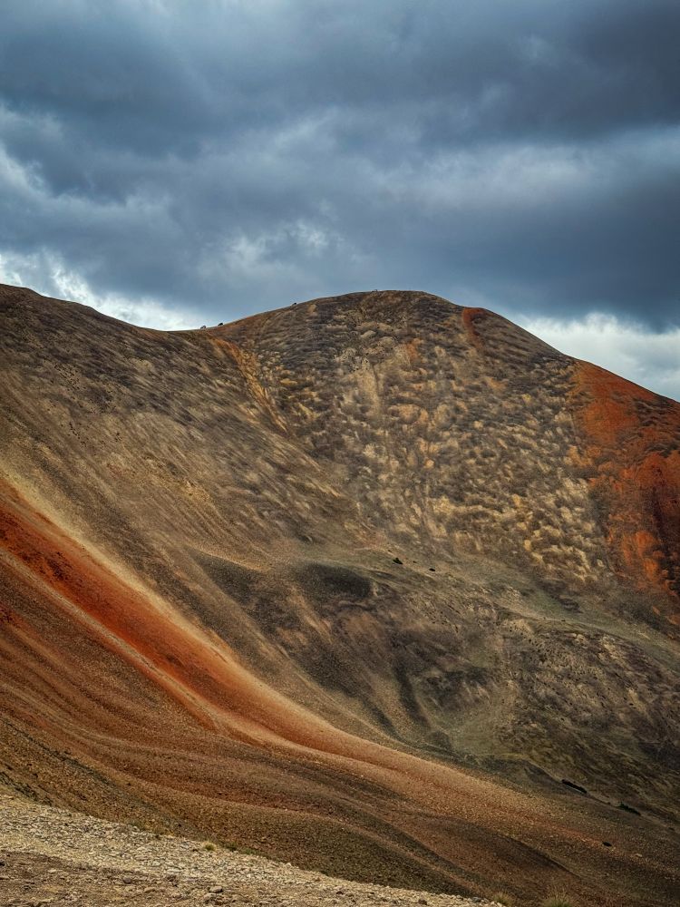 A picture of Red Cone pass in Colorado. Therefore off-road vehicles that can be seen as tiny ant-sized specs along the ridge line. The mountain is awash with deep red stone from the iron ore rusting in the weather. 