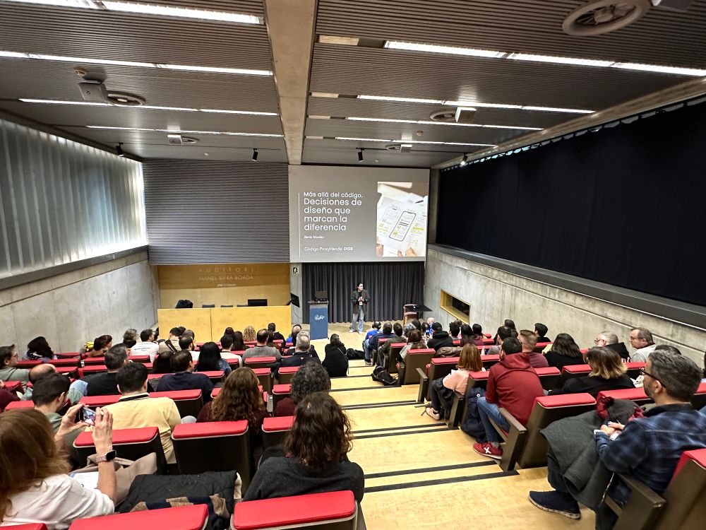 Berta Nicolau en el escenario del auditorio de la a11yConf 2025 en Gerona hablando de diseño y accesibilidad digital delante de la audiencia, en un plan más amplio con la sala llena de asistentes