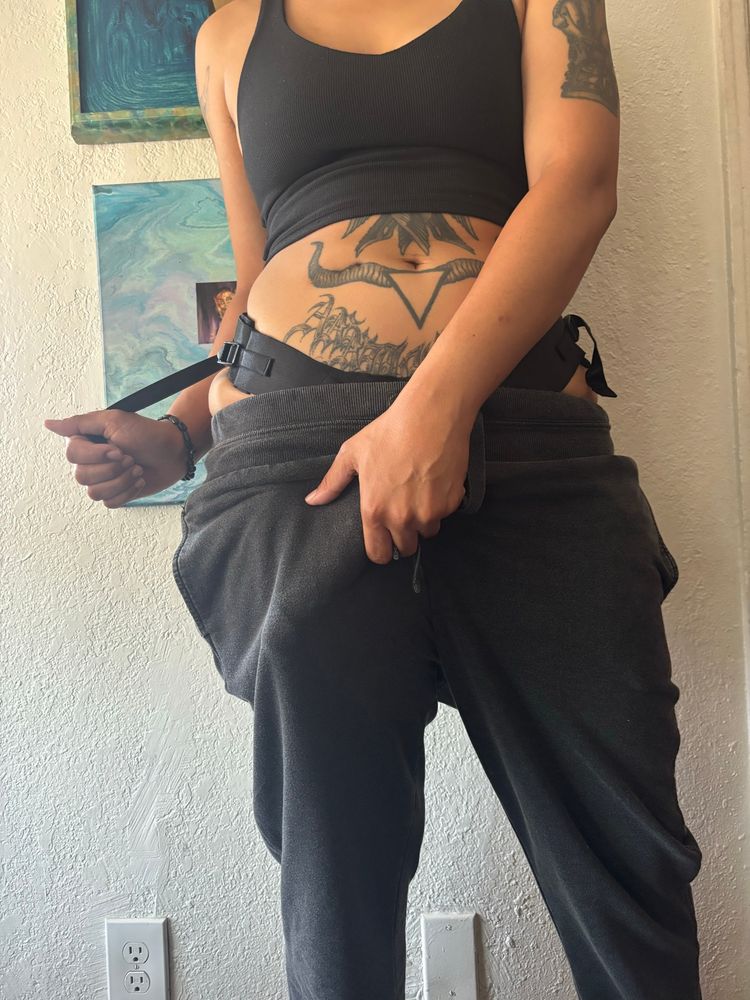 Mae shows off their strap print grey sweatpants