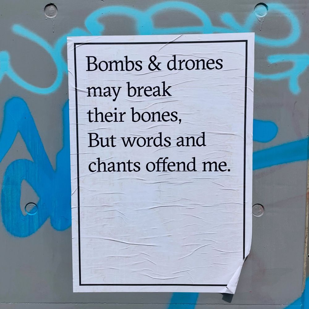 Poster reads, “Bombs & drones may break their bones, But words and chants offend me.”
