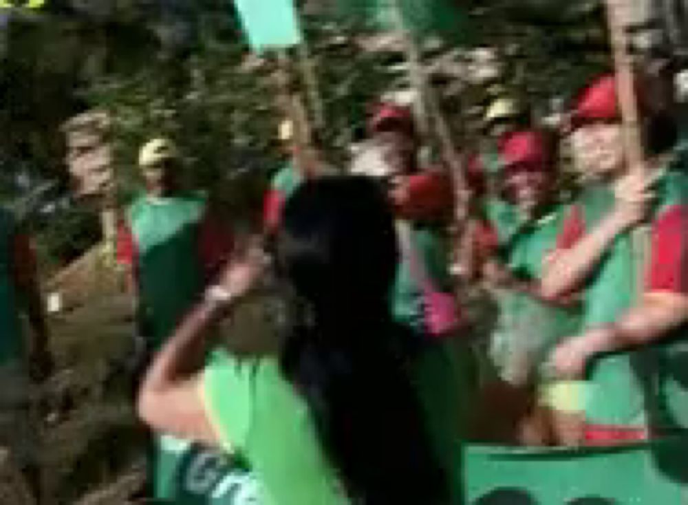 a woman in a green shirt is standing in front of a crowd of people holding sticks .