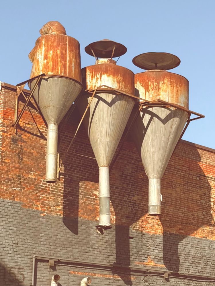 Picture of some rusted mechanical structures attached to the side of a red brick building 