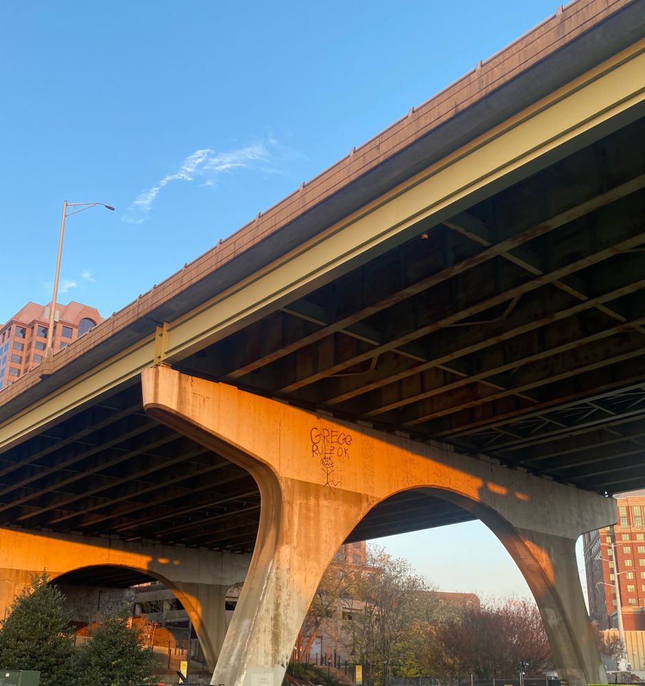 underside of a bridge at golden hour with "GREGG RULZ OK" graffiti and a stick figure 