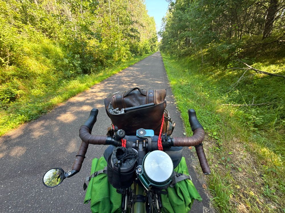 “Cockpit view” of a paved bicycle trail stretching out in front of me into the distance through green wilderness 
