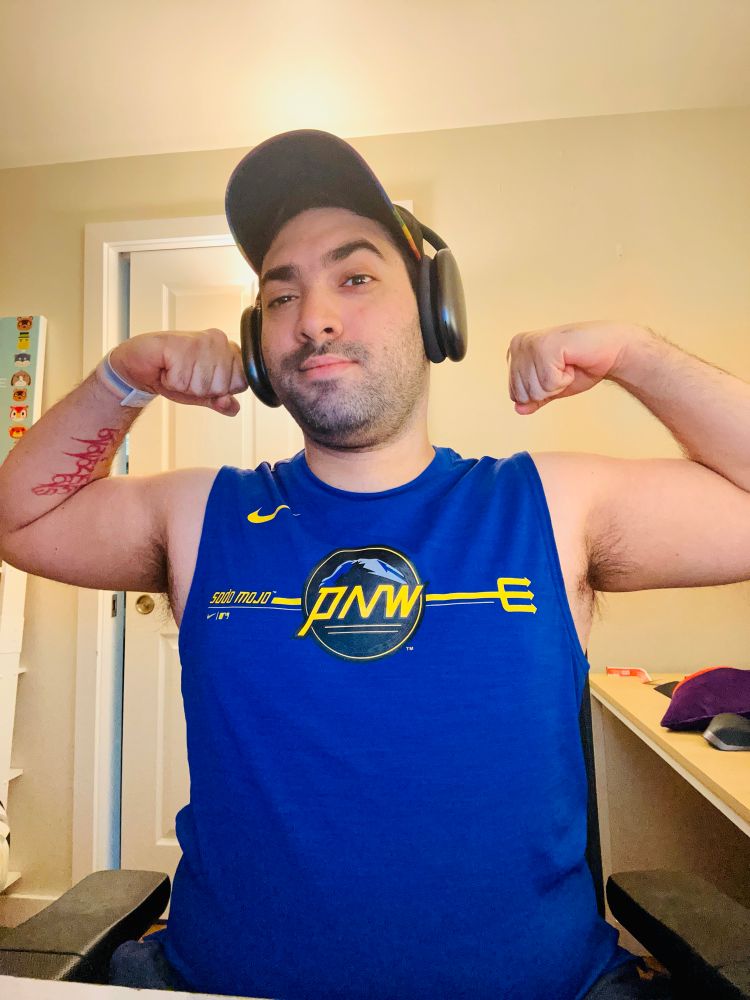 Selfie of me, flexing my biceps in a blue tank top smirking at the camera