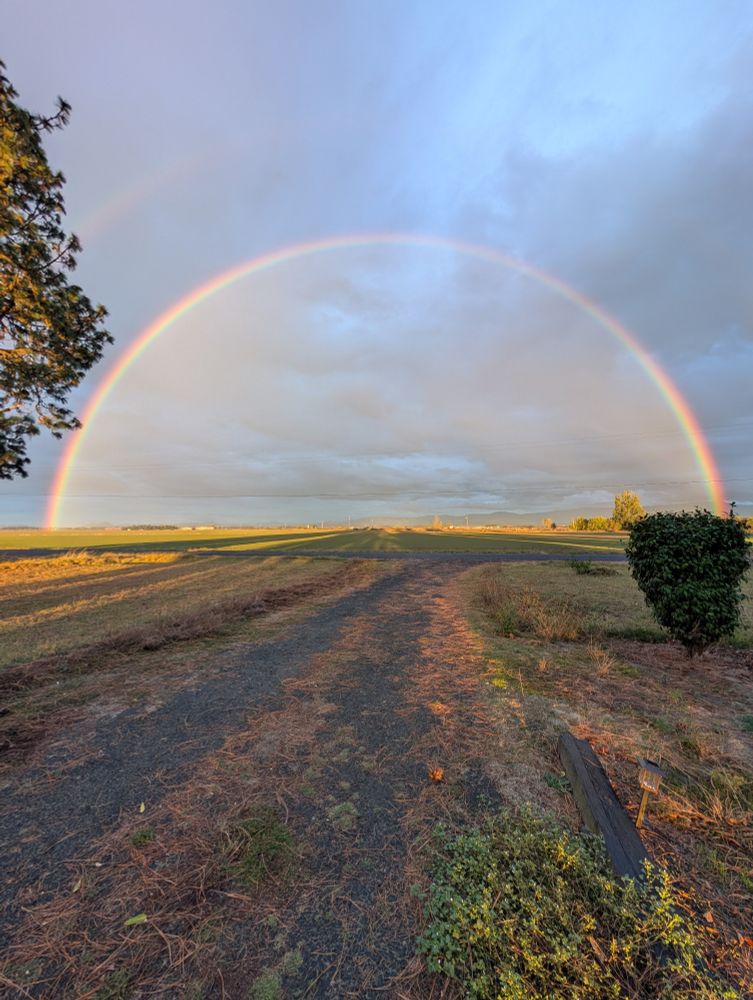 Image of a giant complete rainbow on a field in the country.