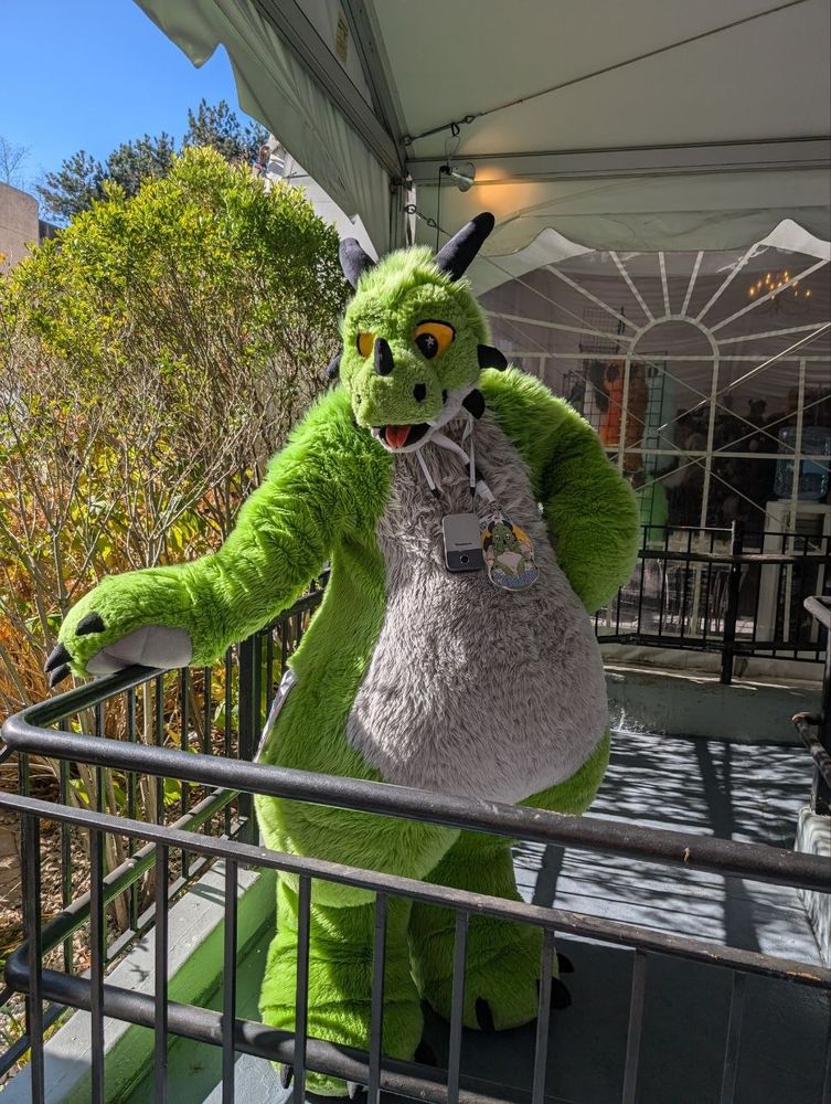 Paradise the plush dragon standing beside a hand rail 