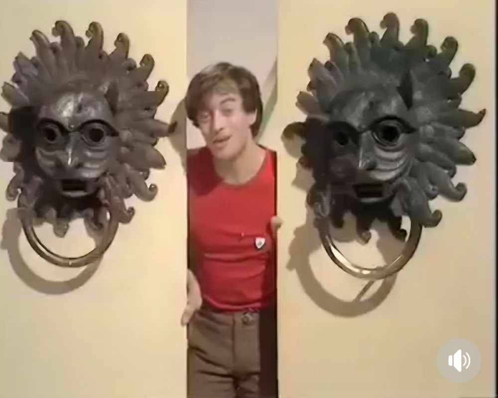 A blue peter presenter standing between a pair of enormous door knockers