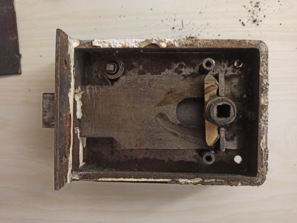 Photo de l'intérieur de la serrure. On voit le penne demi-tour, un petit ressort plat un peu caché, le fouillot (pièce dans laquelle on glisse le carré des poignées pour actionner l'ensemble) 