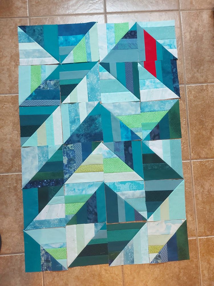 24 blue green and teal half dark and half light HST squares on a floor in a random pattern