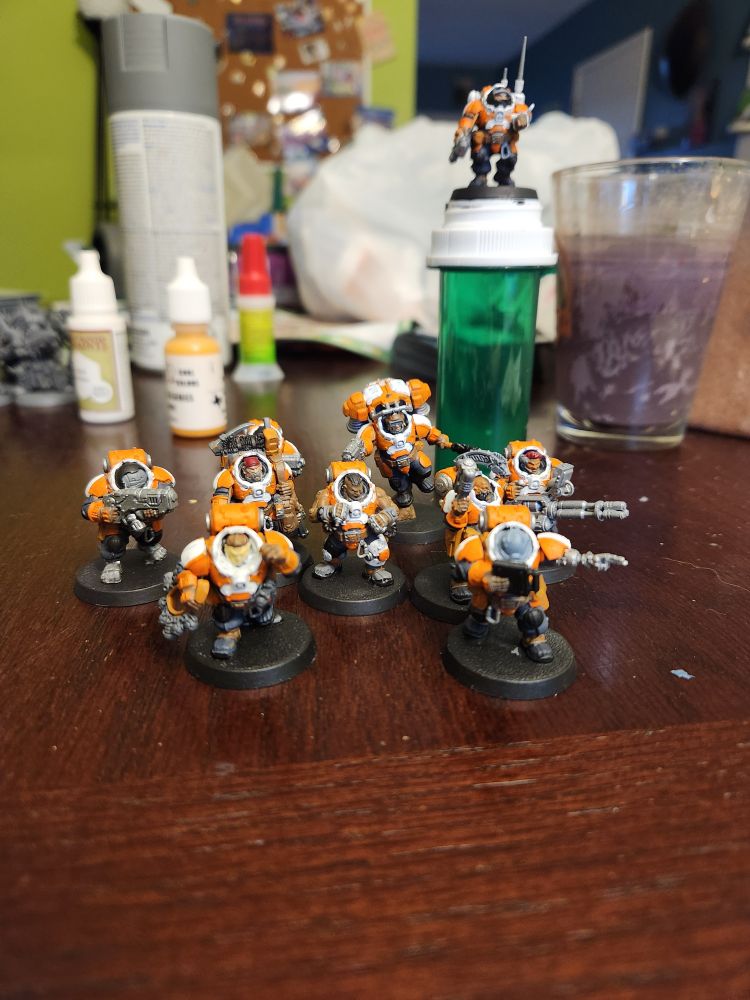 A crew of plastic miniatures with orange and white armor in a variety of battle poses.