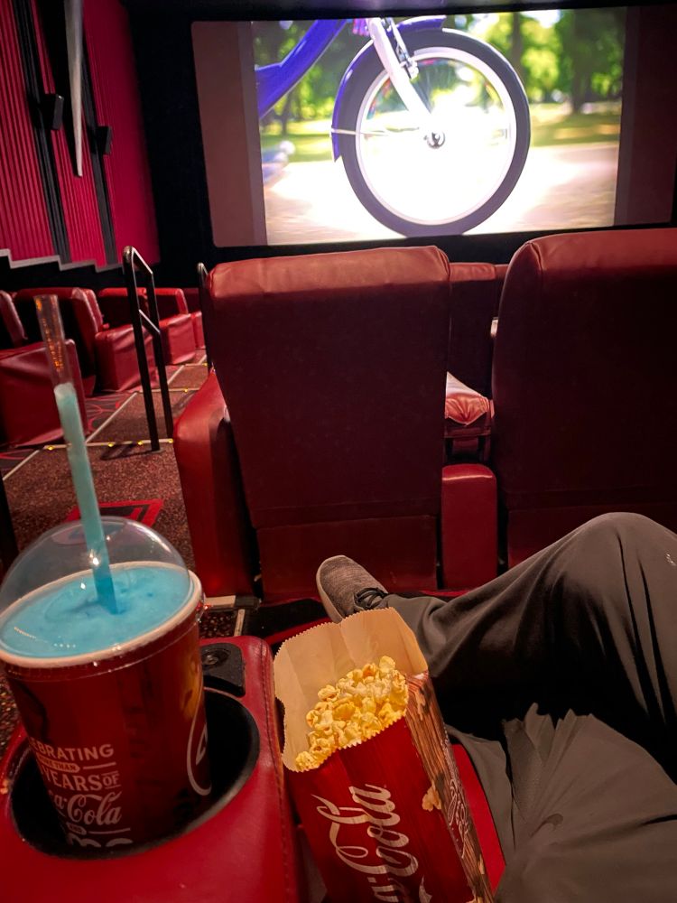 A picture of Smirky sitting in a movie theater chair, featuring a small popcorn and a small ICEE.