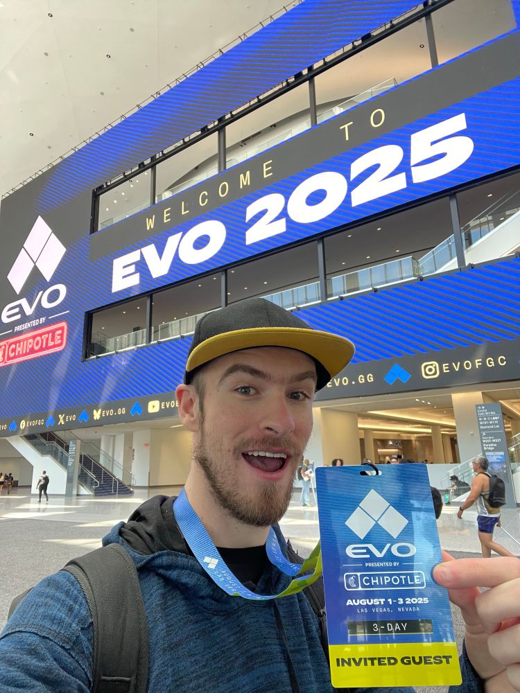 Smirky standing in the West Hall Lobby at the Las Vegas Convention Center, holding up an EVO 2025 ‘Invited Guest’ Badge!