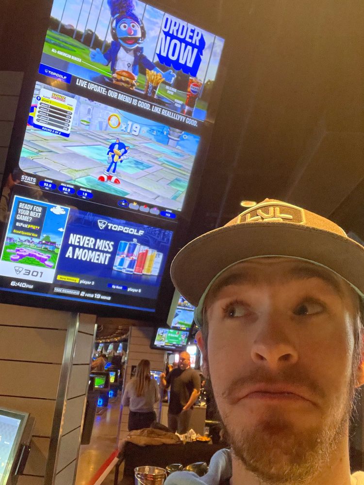 Smirky looks up at a TopGolf monitor featuring… Sonic the Hedgehog!?