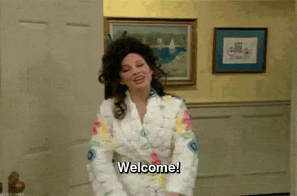 a woman in a bathrobe is standing in a room and says welcome .