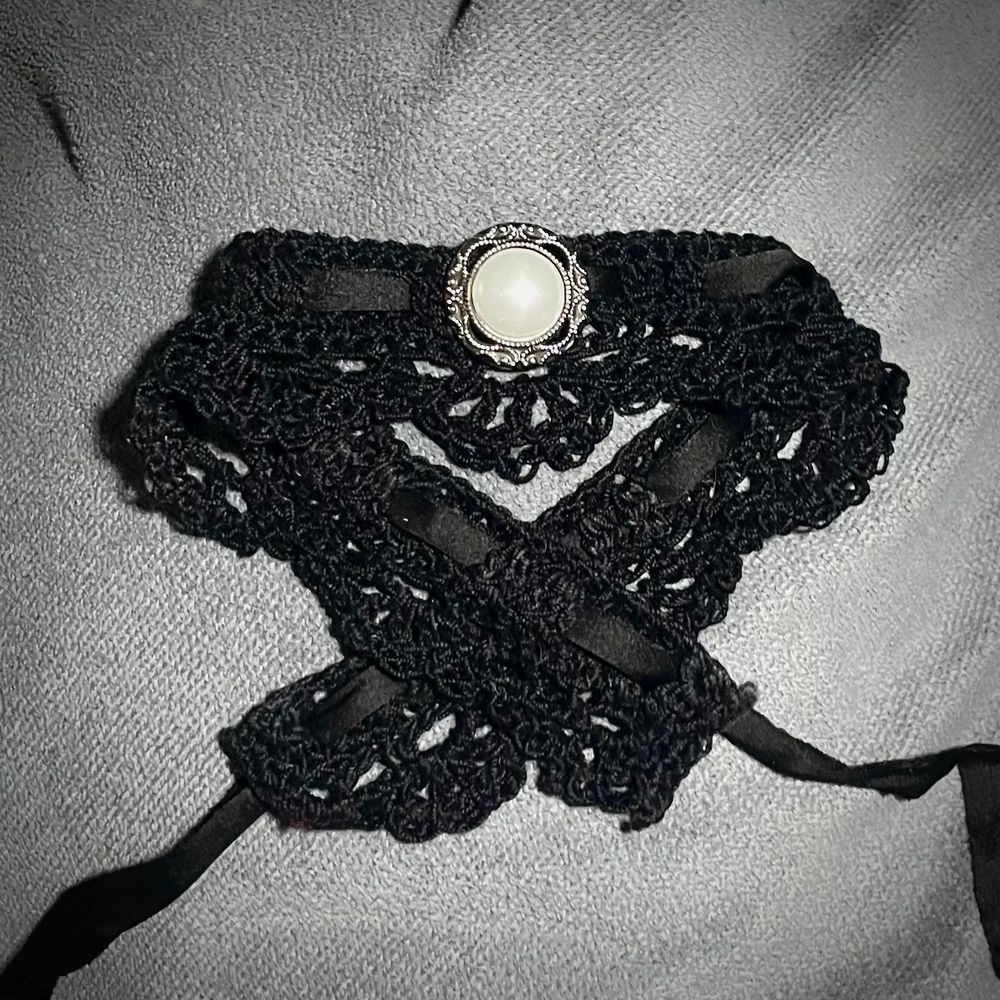 A black lace choker with a pearl colored bead and black ribbon folded on a grey background.