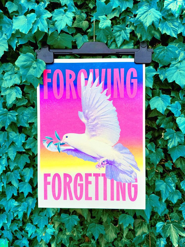 A poster print, attached to a grip hanger, sits against a wall of green ivy. The print depicts a peace dove, mid-flight, with a small olive branch in its mouth - the backdrop is a (top to bottom) blue, pink, yellow gradient, dissolving into a white at the footer of the print. “FORGIVING” heads the design in bold, hot pink type at the very top of the page, behind the dove. “is not” sits in smaller type below, blending into the pink. Then at the very bottom, the same size + colour as the “FORGIVING” header type, it reads “FORGETTING”. The whole phrase being “Forgiving is not Forgetting”. It’s a very vibrant, eye catching print full of warm colours.