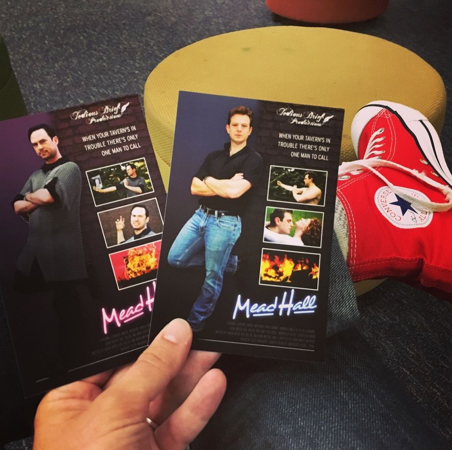My left hand holding the two versions of our Mead Hall (2016 MN Fringe) postcard, each replicating the Road House (1989) movie poster. Left, the one focusing on my character's 1-man Beowulf show. Right, the one focusing on the fictitious "Road House: The Musical" Fringe show.