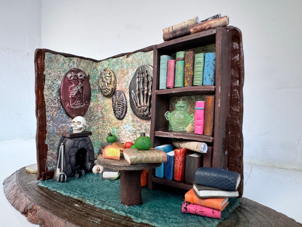 Maqueta de una habitación, se ven imágenes algo macabras en las paredes y muchos libros