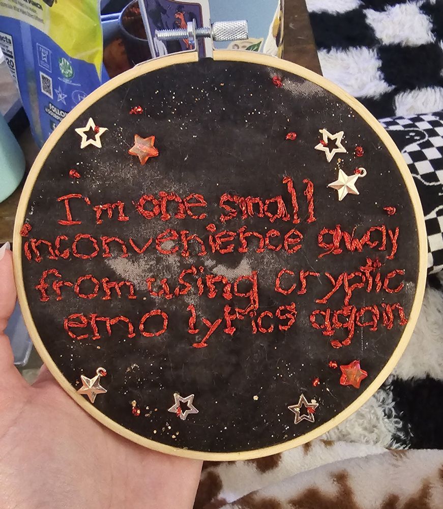 Embroidery piece with black fabric background with red font, gold metallic stars, red star beads and gold glitter